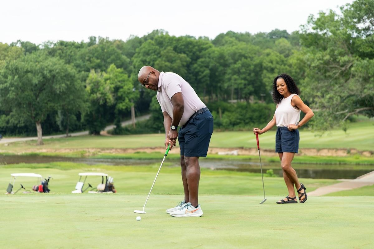 Man putting on golf green, woman watching with a smile.