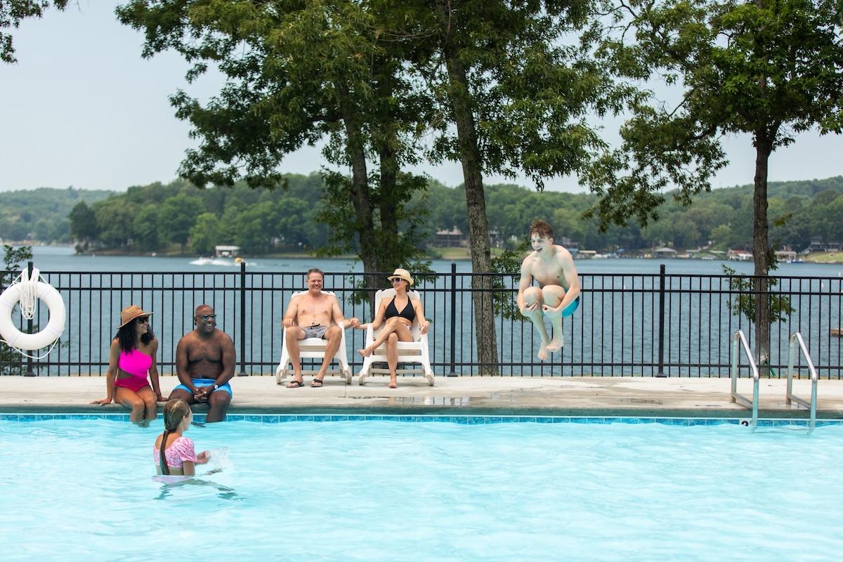Poolside relaxation by a lake with a child swimming and a person mid-air jumping in.