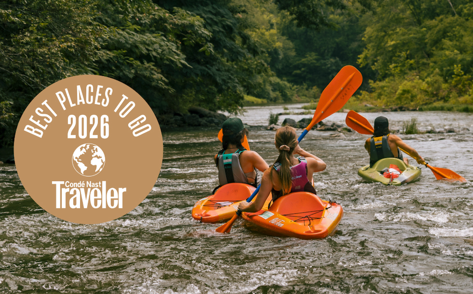 Kayakers paddling down a forested river with an award badge on the side.