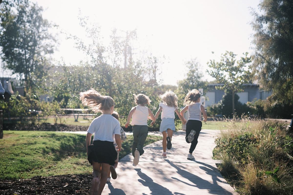 Children running on a sunlit path in a park setting.