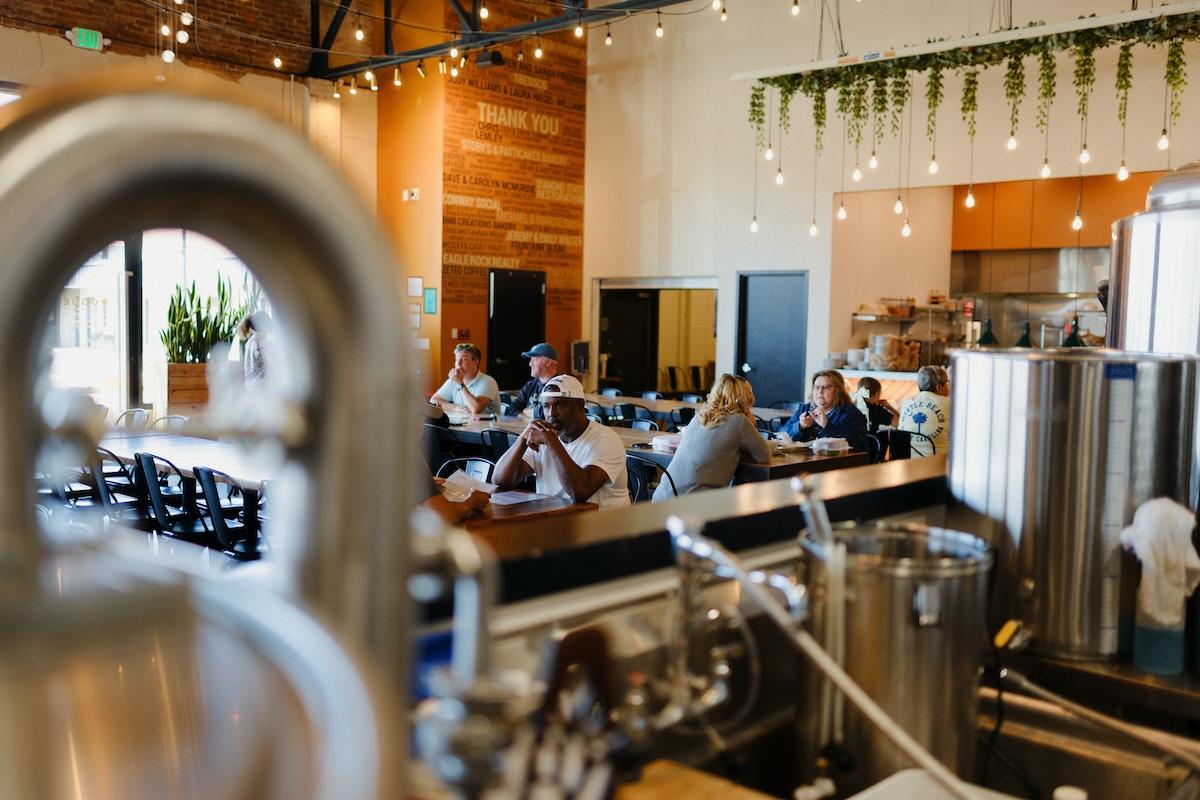 Brewery interior with patrons seated at tables under hanging lights.