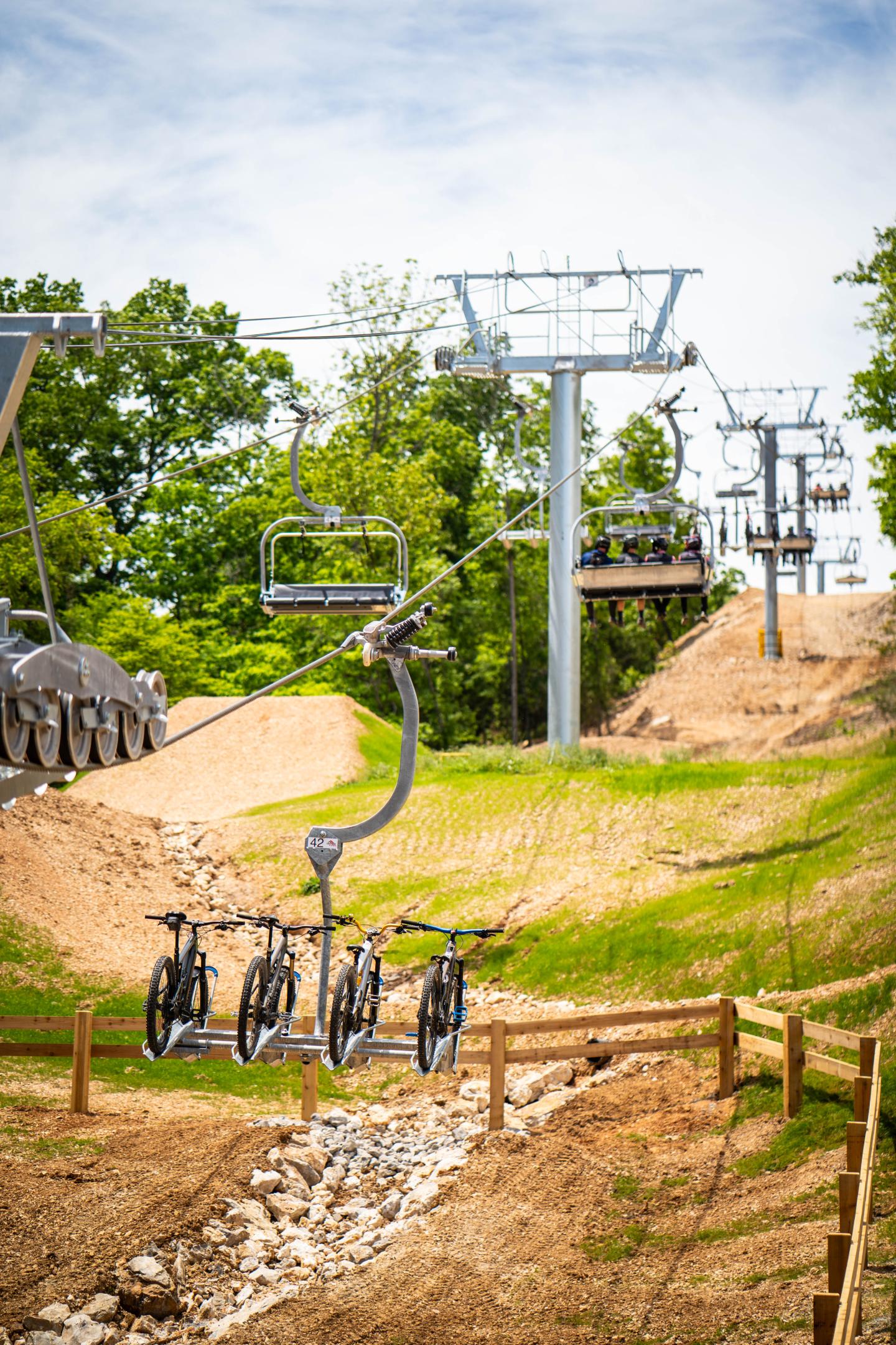 Bicycles on a ski lift, green trees, and hilly dirt paths.
