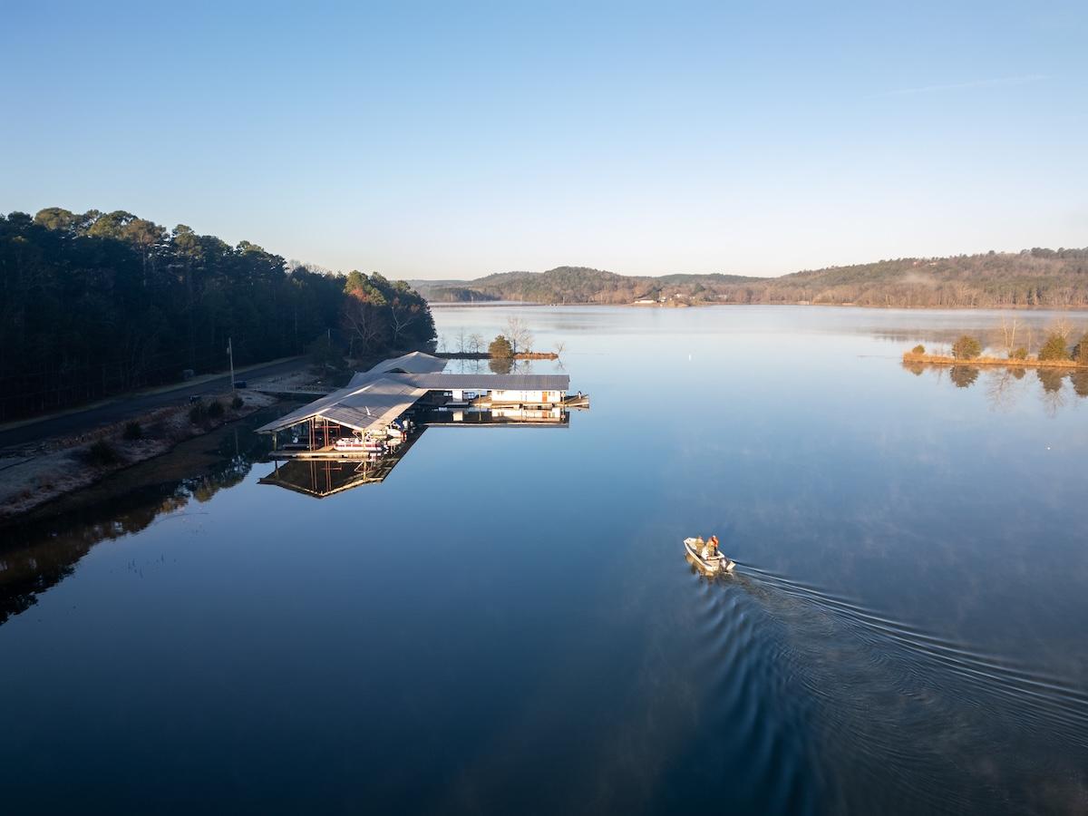 Calm lake at sunrise with small boat and distant docks.