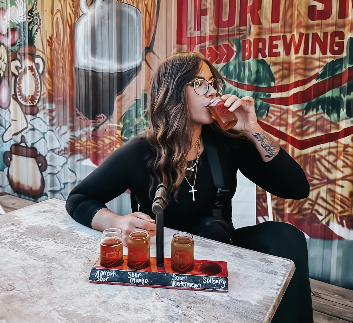 Woman drinking beer at a brewery, seated at a table with beer samples.