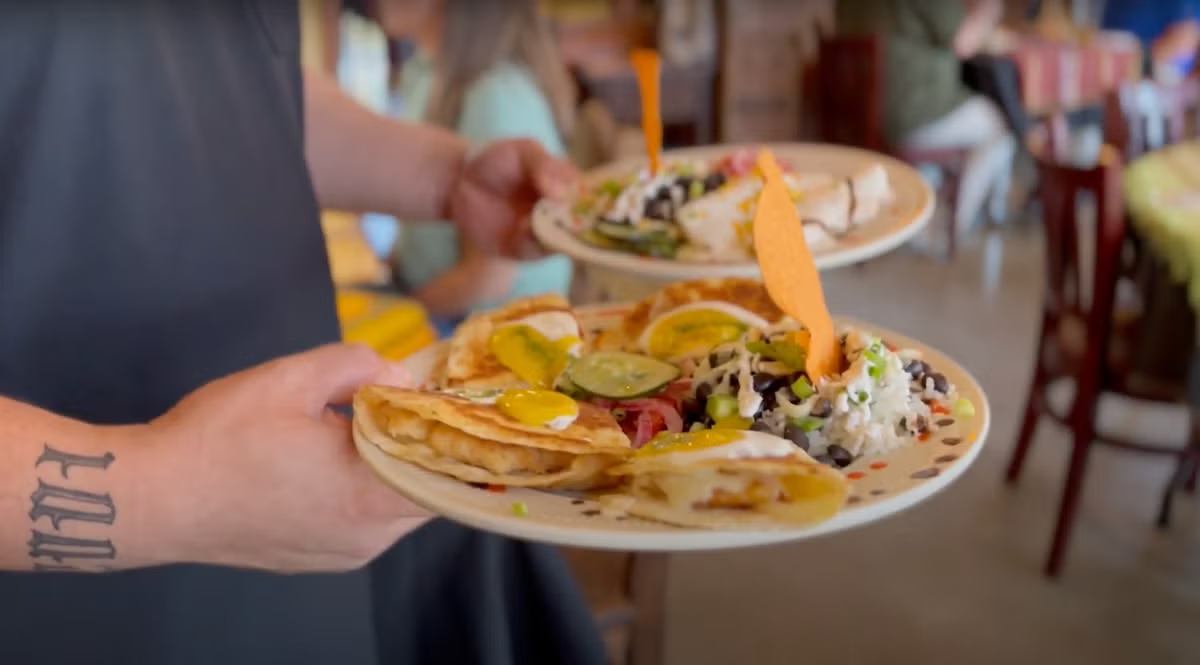 Server holding plates of tacos with various toppings in a restaurant.