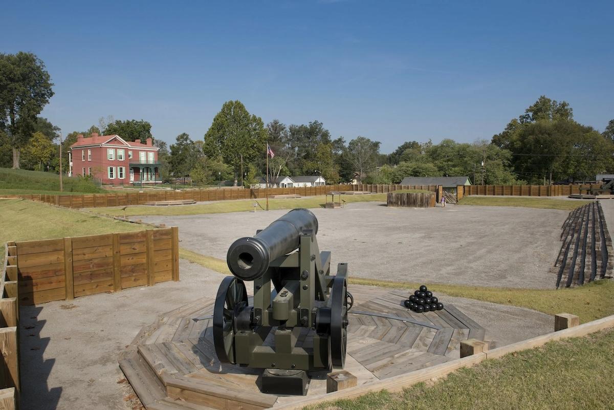 Historic site with a cannon on display, surrounded by grassy area and trees.