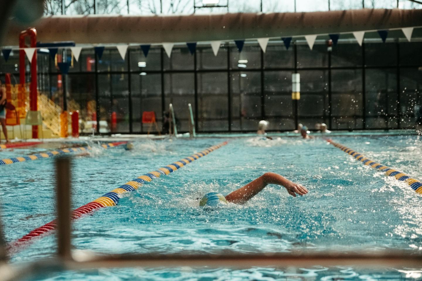Indoor pool with a swimmer in mid-stroke, colorful lane dividers.