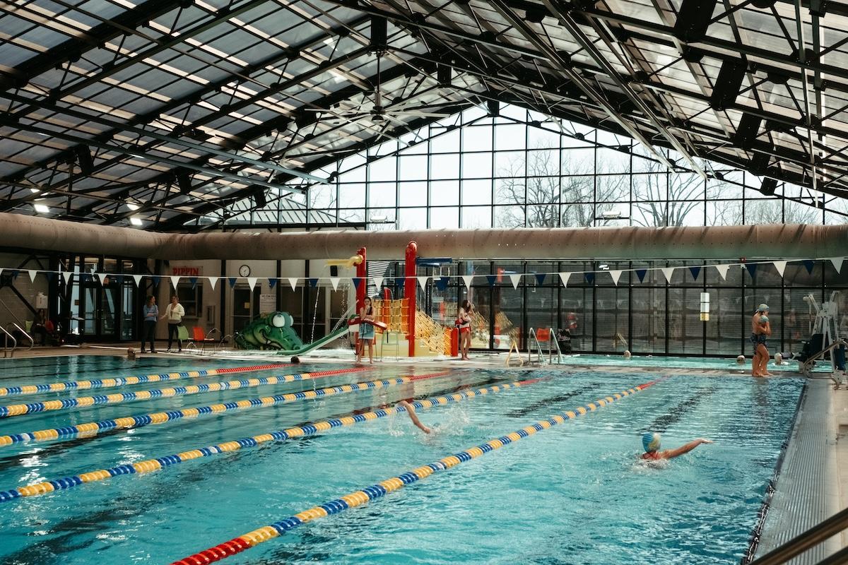 Indoor pool with swimmers, glass ceiling, and colorful lane dividers.