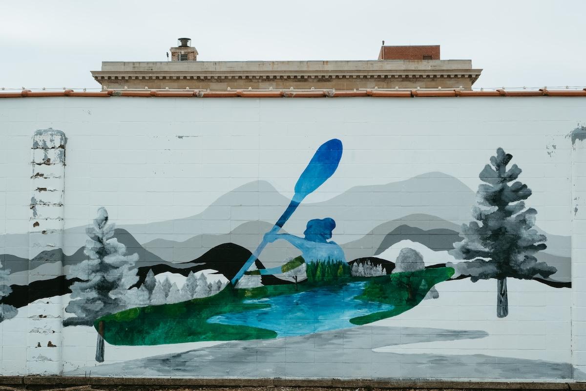 Mural of a kayaker on a blue lake with mountains and trees.