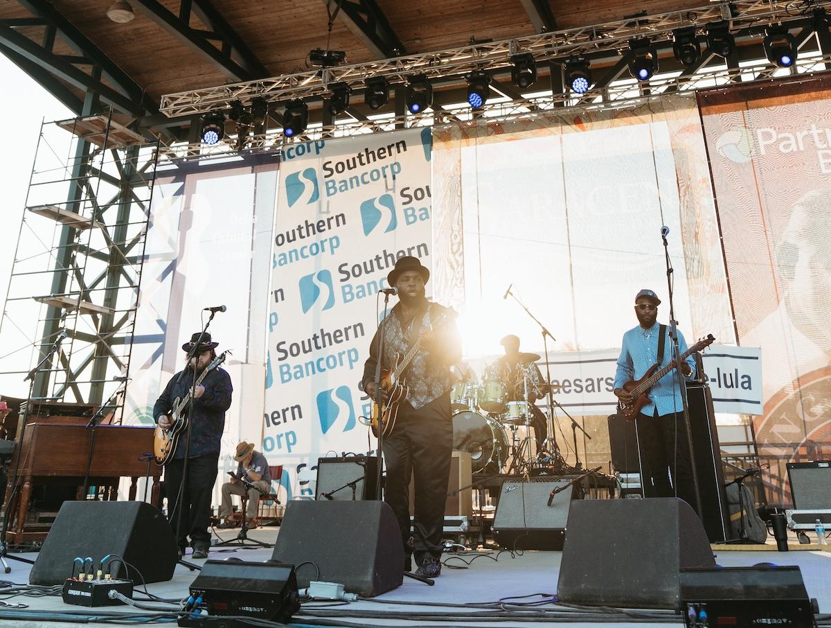 Band performing on an outdoor stage with evening sunlight.