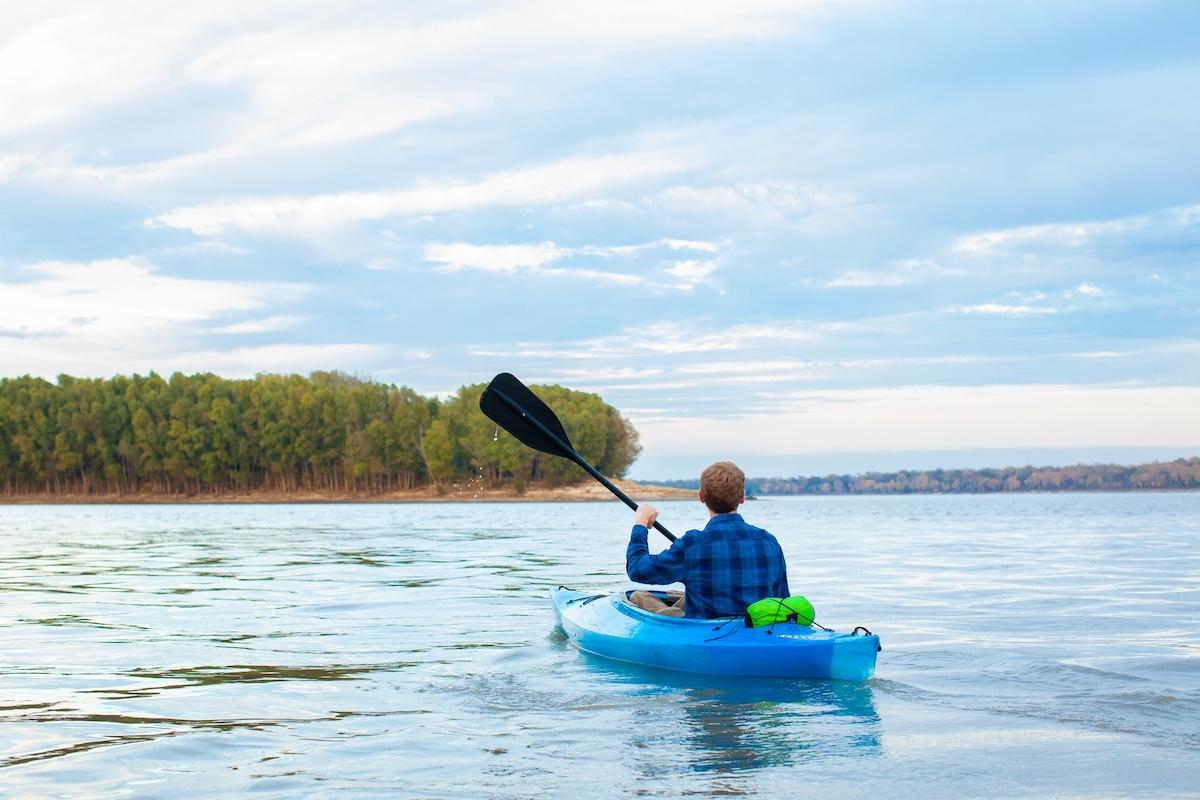 Person kayaking on a calm lake under a cloudy sky.