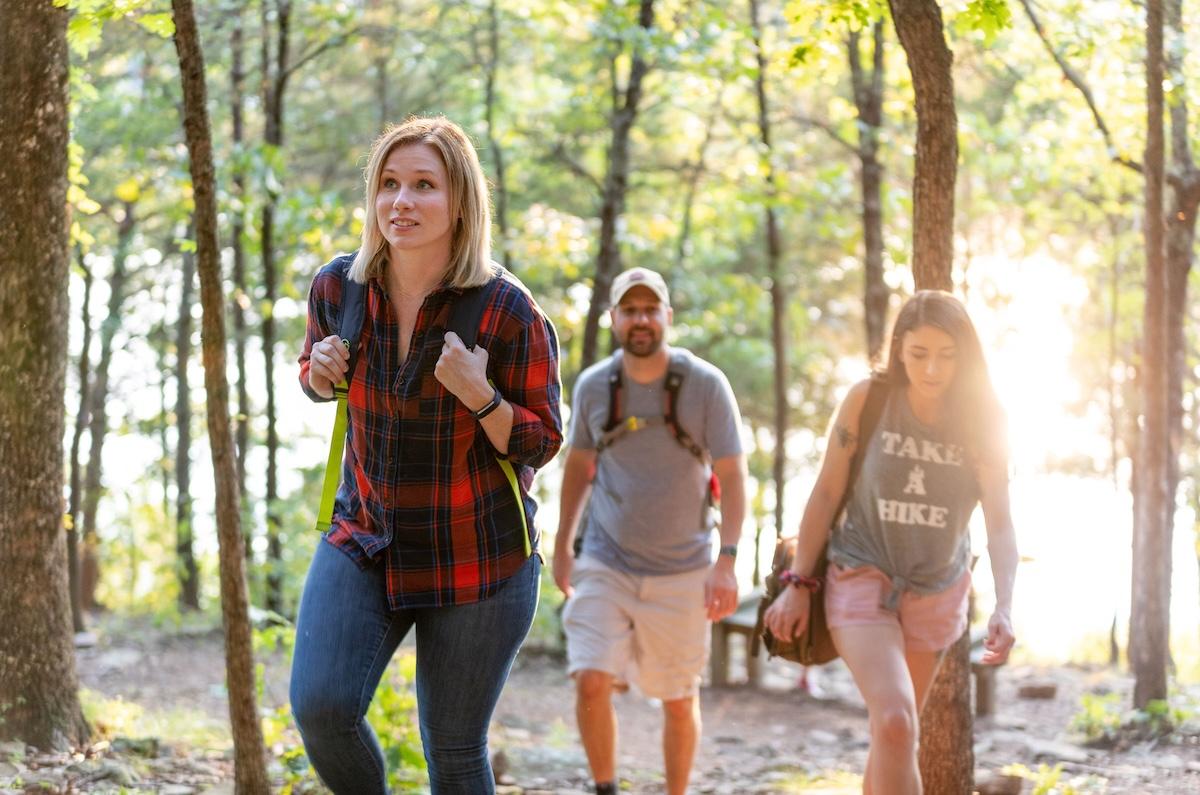 Three people hiking on a forest trail in sunlight.