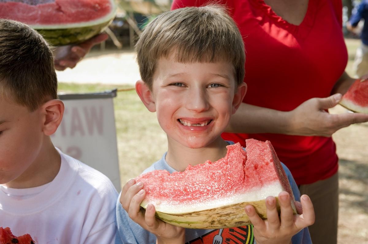 Smiling boy holding a slice of watermelon outdoors.