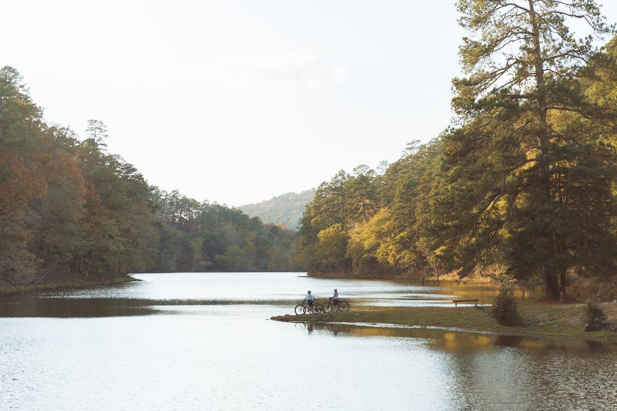 Calm lake with two people on a narrow bridge, surrounded by autumn trees.