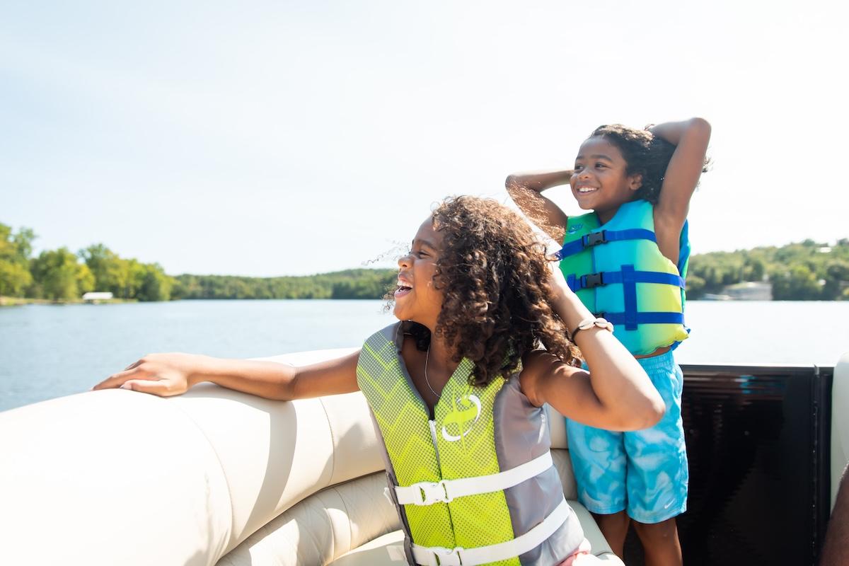 Two children in life vests smiling on a boat, sunny day.