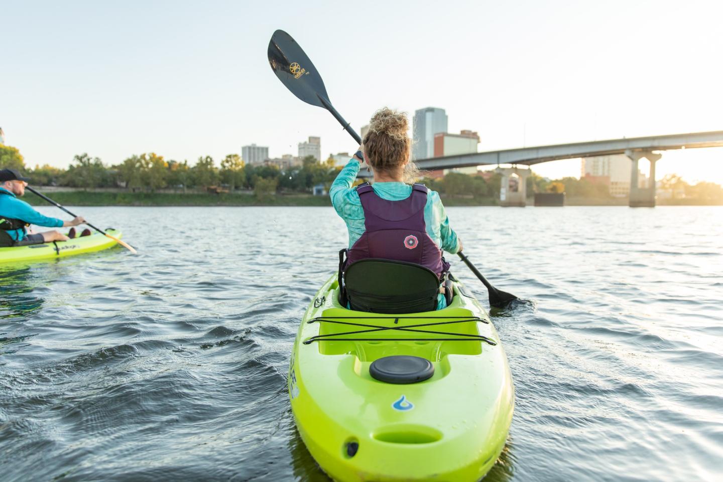 Person kayaking on a river with city skyline in background.