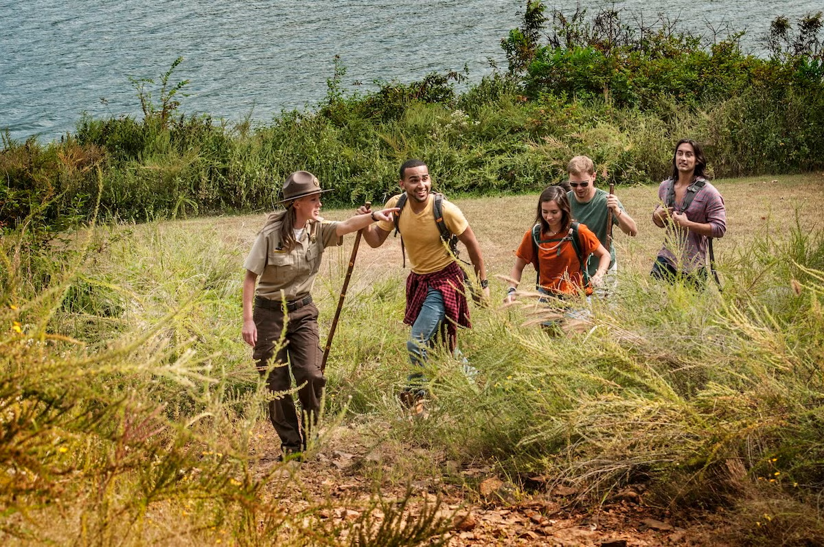 Group hiking up a grassy hill near a lake, led by a guide with a walking stick.