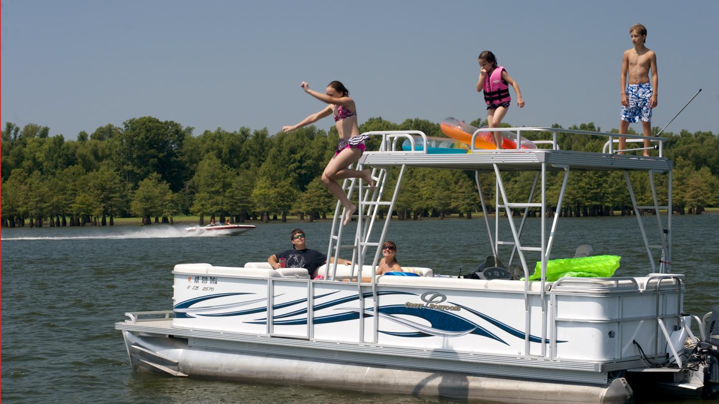 People jumping off a pontoon boat into a lake on a sunny day.