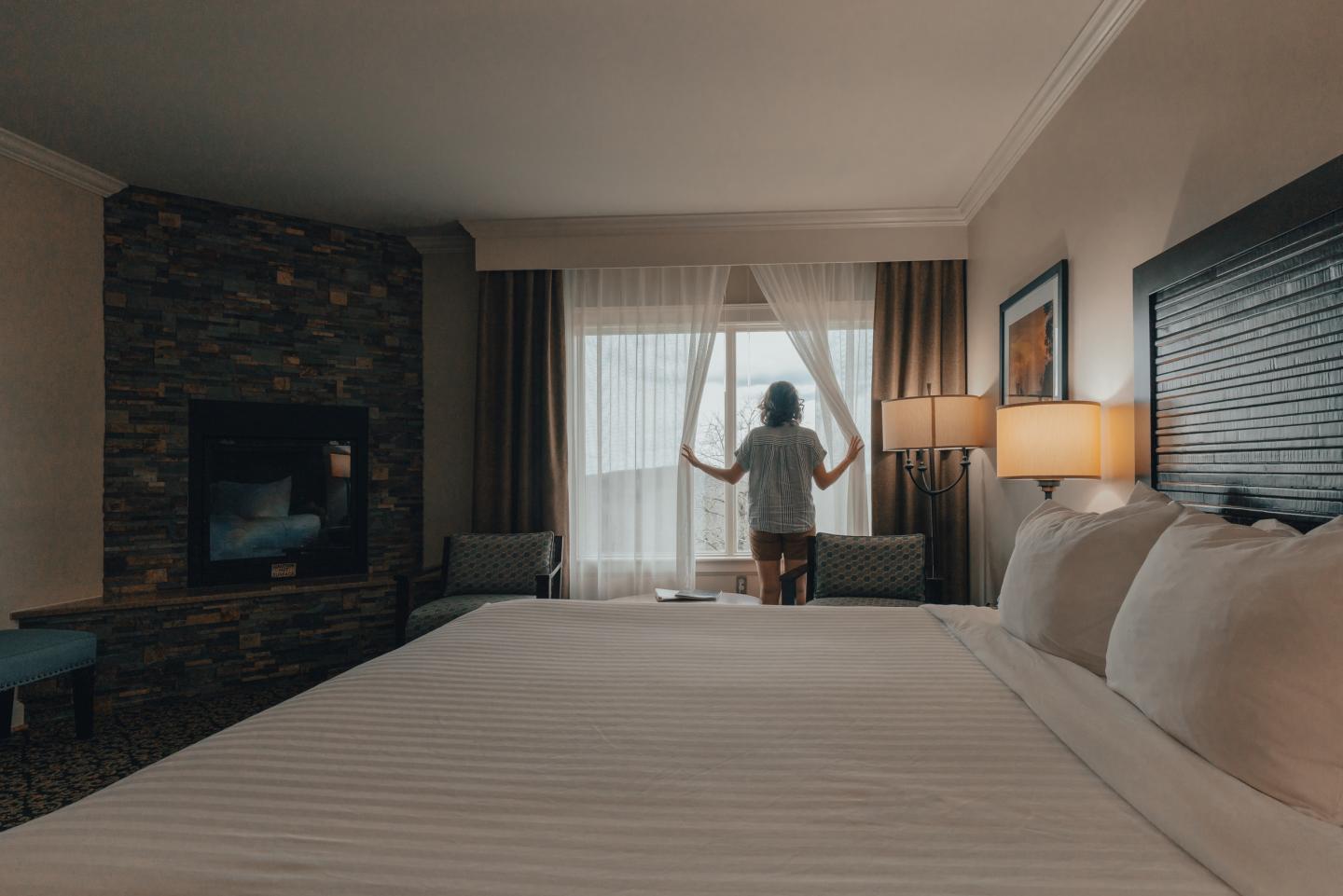 Person stands by a hotel window, light filters through curtains.