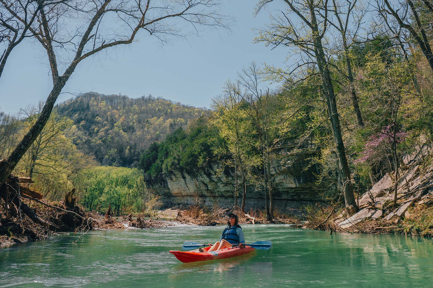 Person kayaking on a calm river surrounded by trees and hills.
