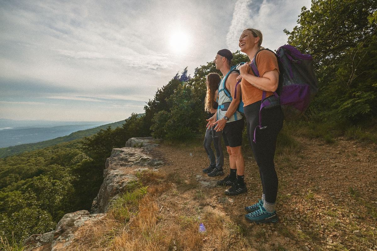 Hikers with backpacks enjoying a scenic mountain view under a bright sun.