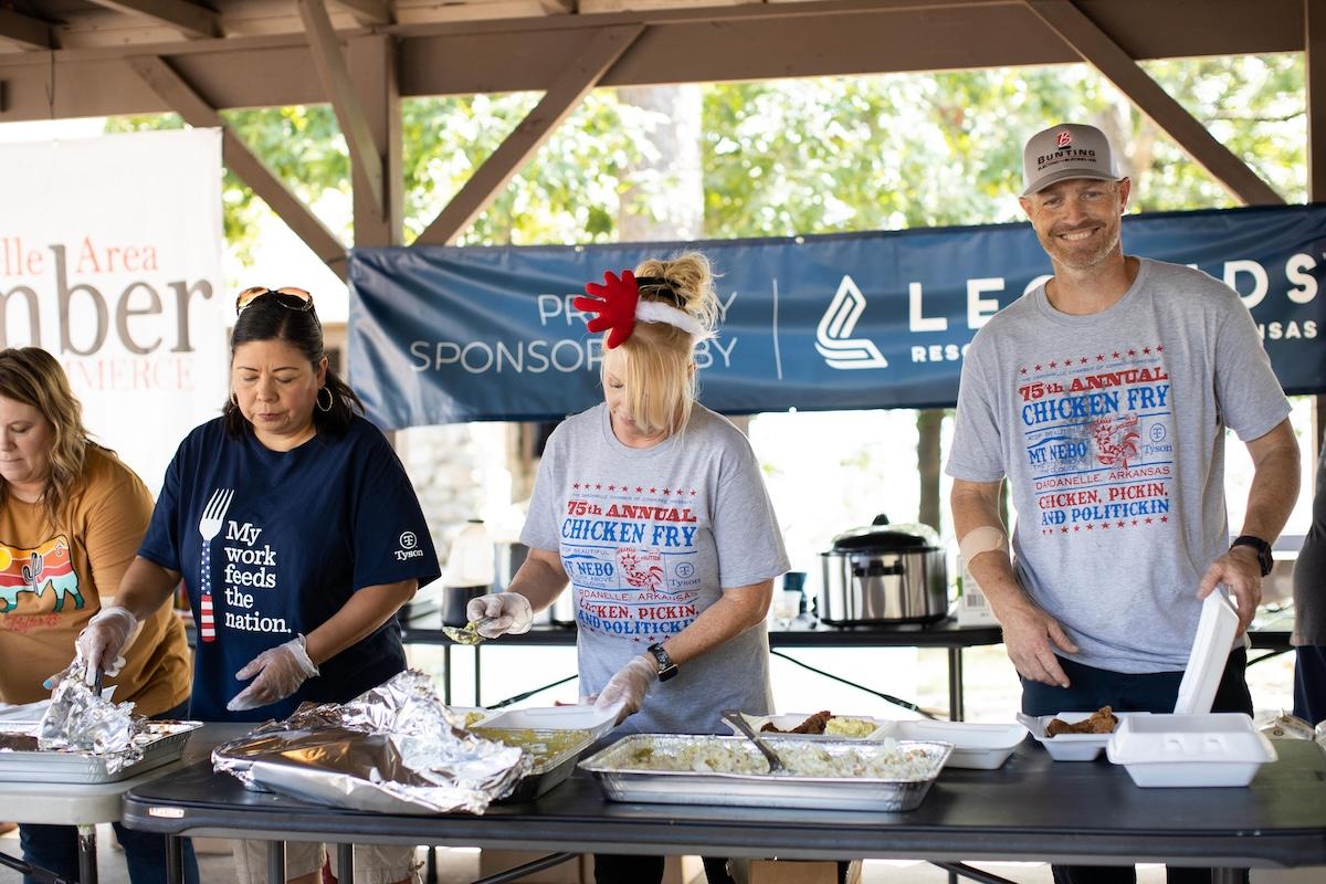 People serving food at an outdoor event under a pavilion.