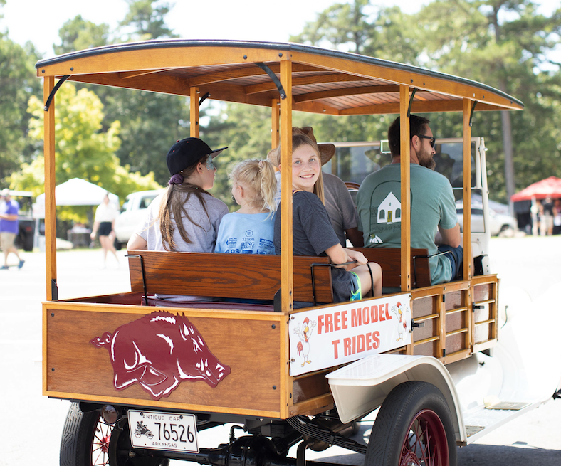 People riding in an open wooden trolley on a sunny day.