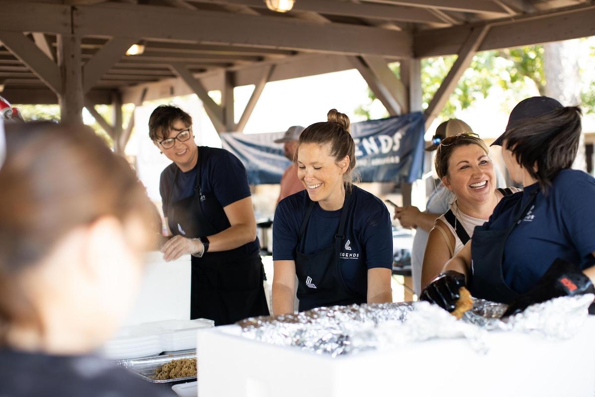 People serving food outdoors, smiling and interacting.