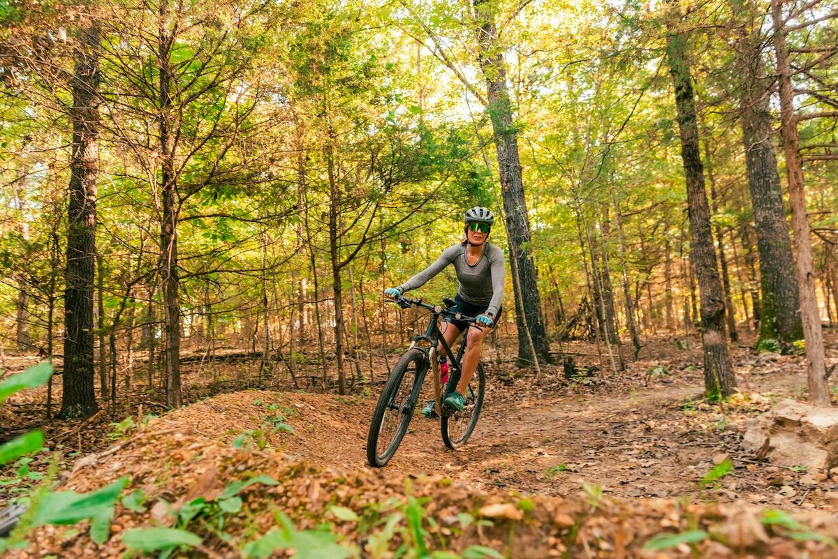 Cyclist riding through a sunlit forest trail in autumn.