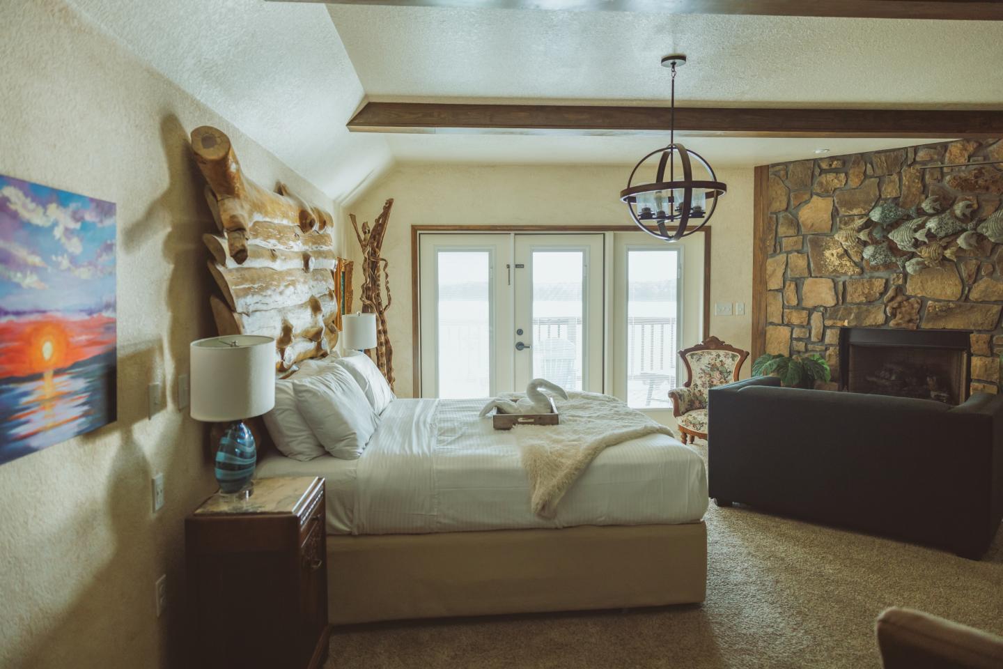 Cozy bedroom with a bed, stone fireplace, and large windows.