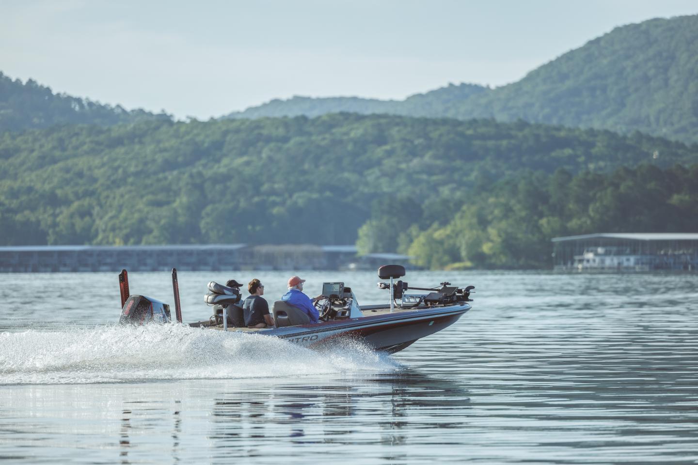 A boat speeding on a lake with tree-covered hills in the background.