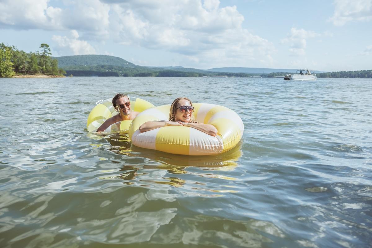 Two people relax on inflatable tubes in a sunny lake.