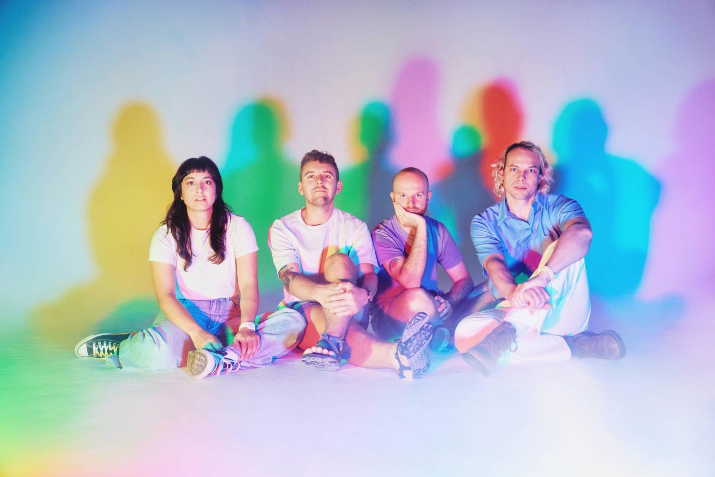 Four people sit on the floor with colorful shadows behind them.