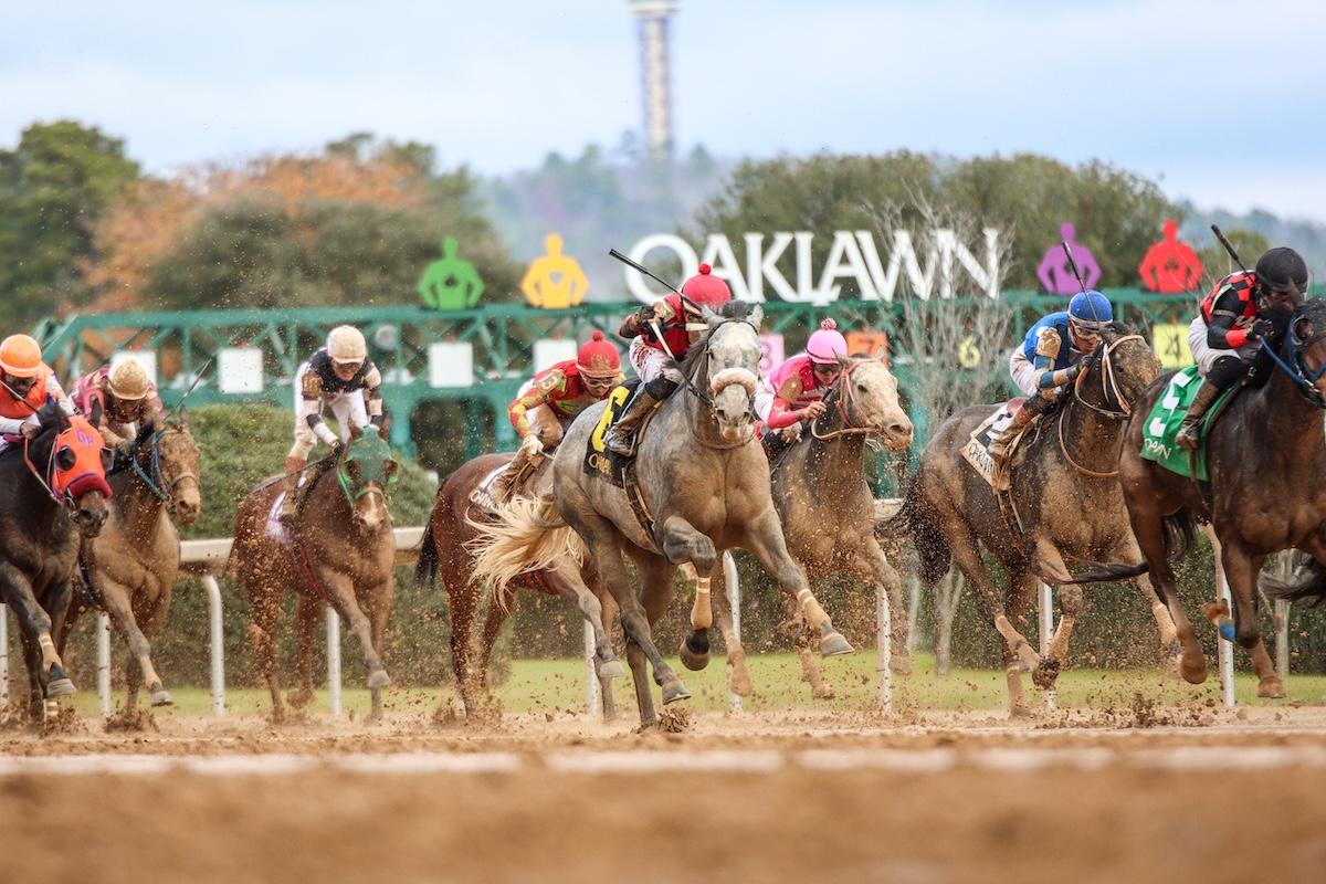 Horses racing on a muddy track at Oaklawn, jockeys in colorful silks.