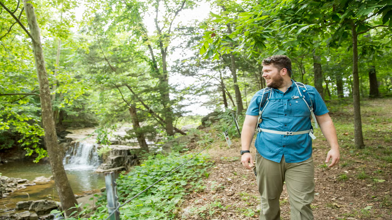 Man hiking on a forest trail near a small waterfall.