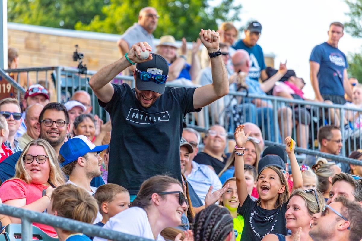 Crowd cheering at outdoor event, man raising arms joyfully.
