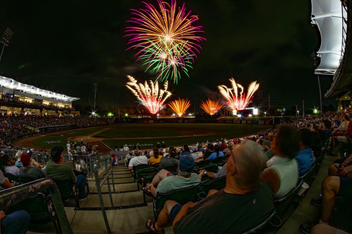 Fireworks light up the night sky over a crowded stadium.