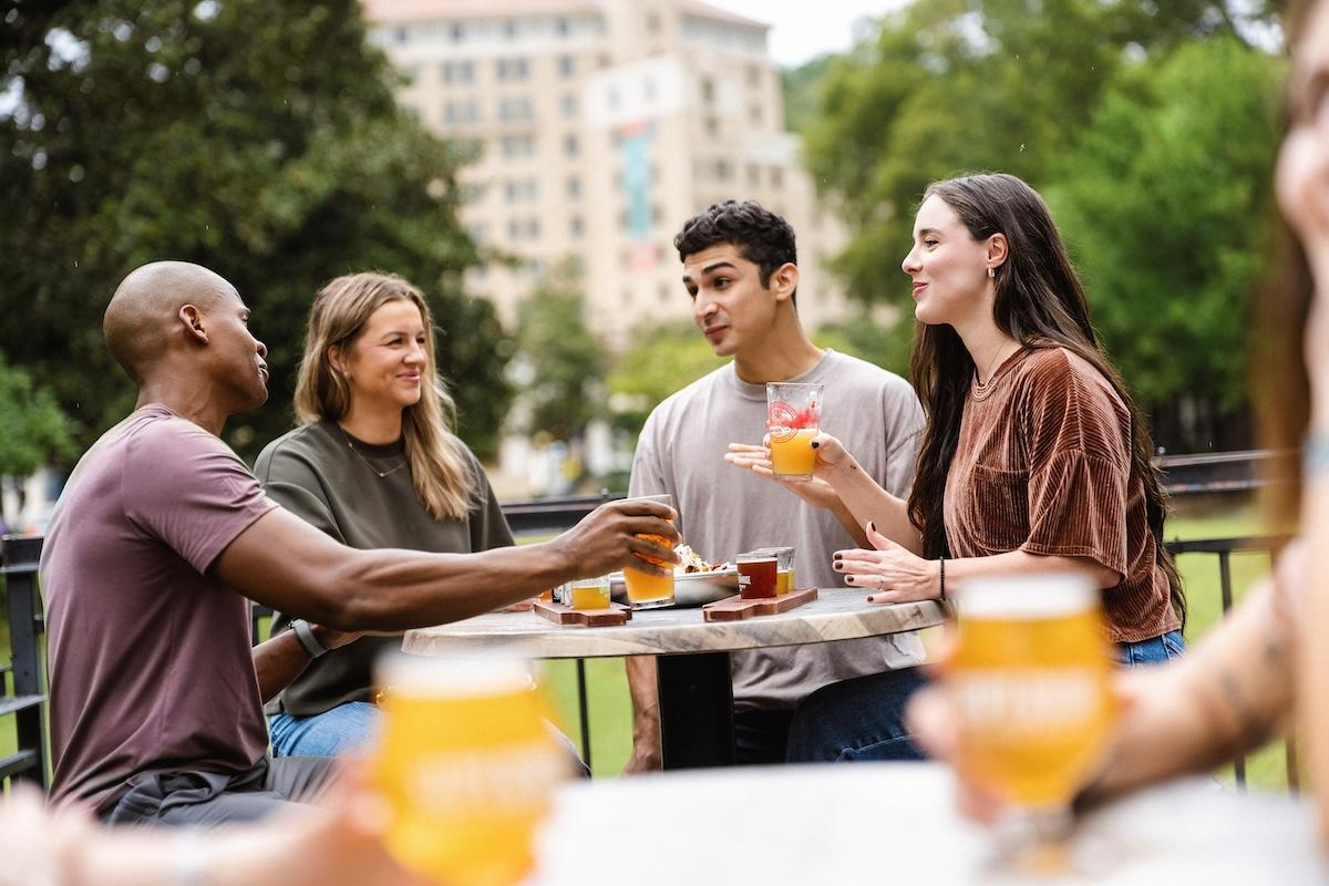 Four friends smiling and chatting at an outdoor table with drinks.