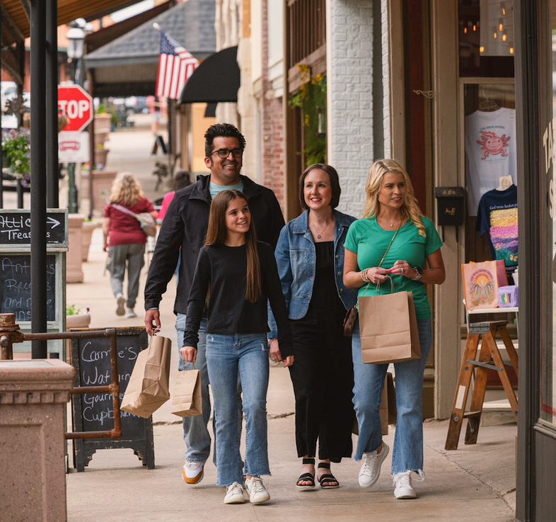 Four people walking on a sidewalk, carrying shopping bags, smiling.