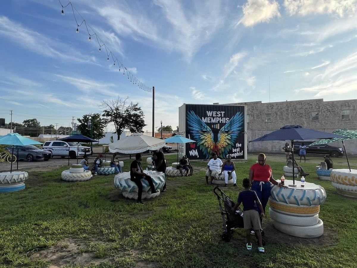 People relax on colorful tire seats in a grassy outdoor area under string lights.