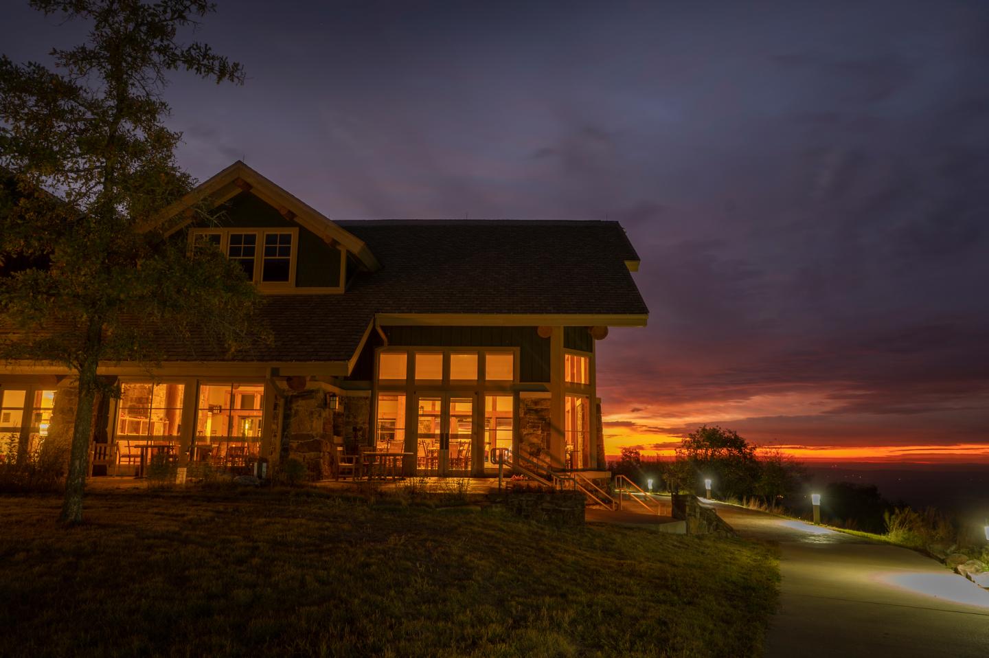 Cozy house with glowing windows, surrounded by a vibrant sunset.