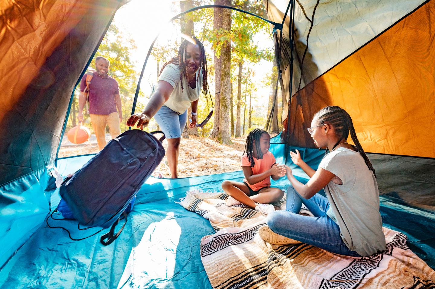 Family setting up a tent in the forest, children playing inside.