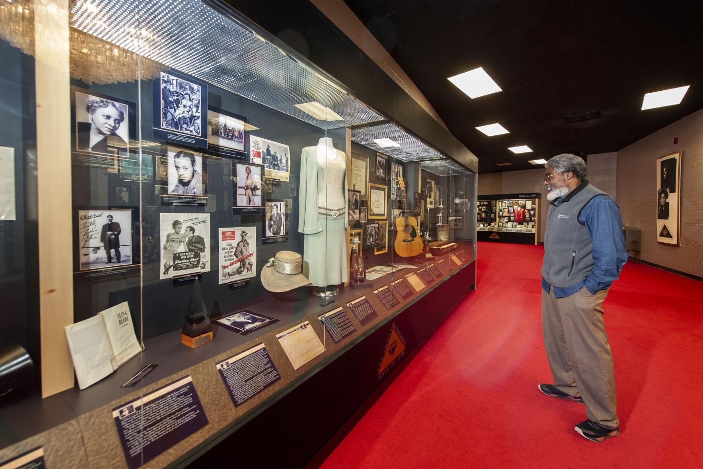 Man observing museum exhibit with photos and memorabilia in a glass case.