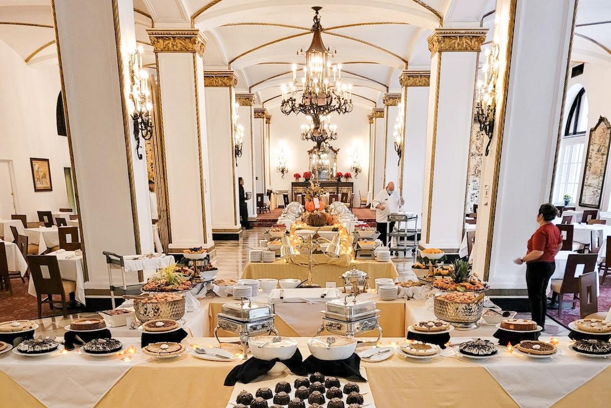 Elegant buffet in a grand dining hall with chandeliers and white columns.