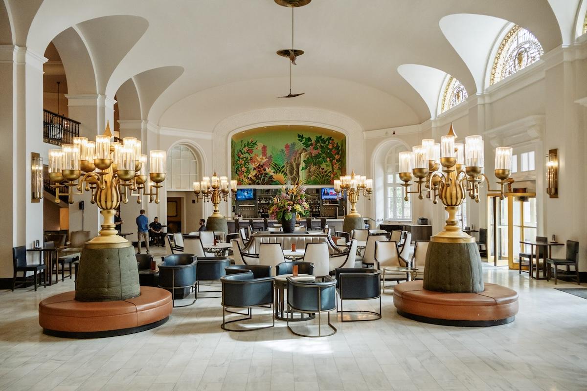 Grand hotel lobby with chandeliers and arched windows.