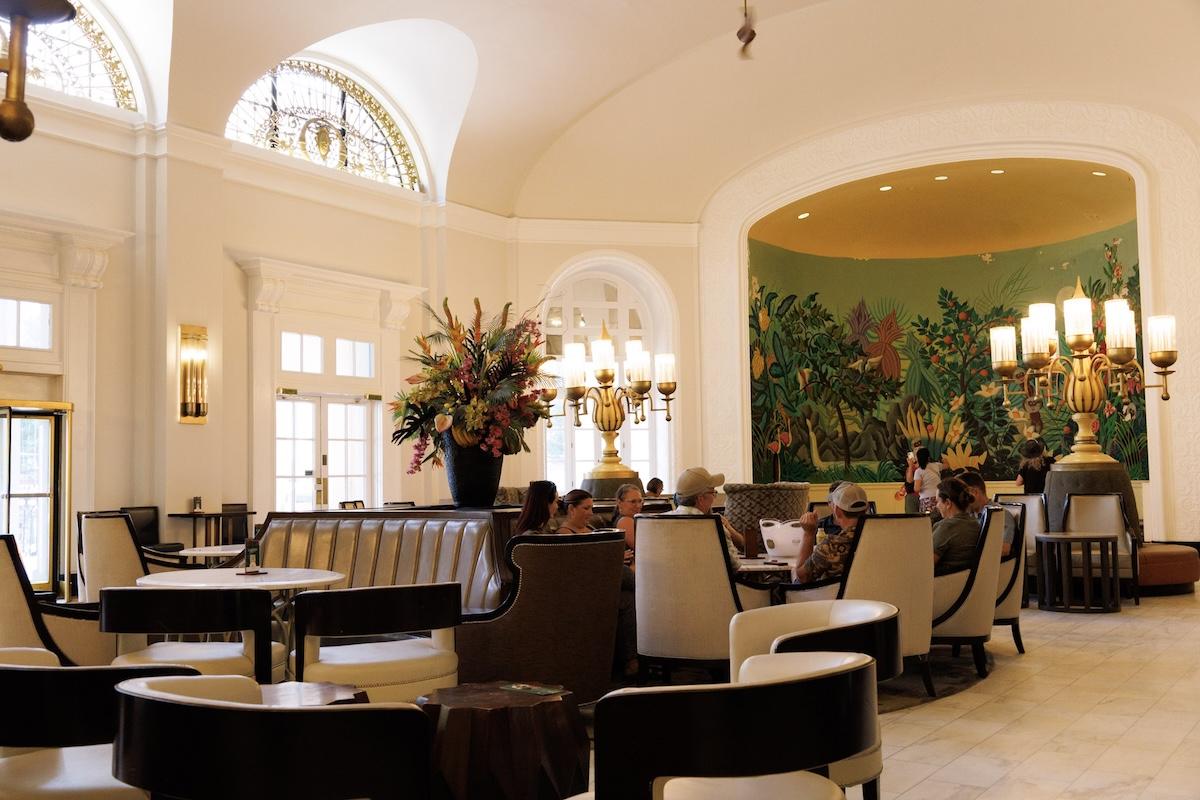 Elegant hotel lobby with plush seating, mural, and floral arrangement.