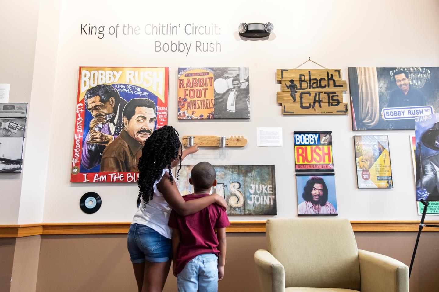 Children observe a wall display of Bobby Rush posters and memorabilia.