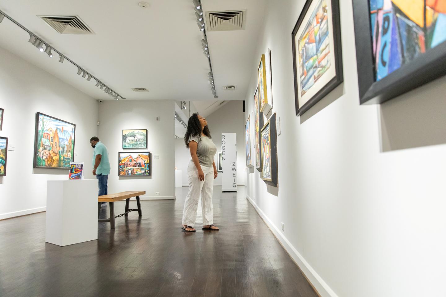 Art gallery visitors observing colorful paintings on white walls.