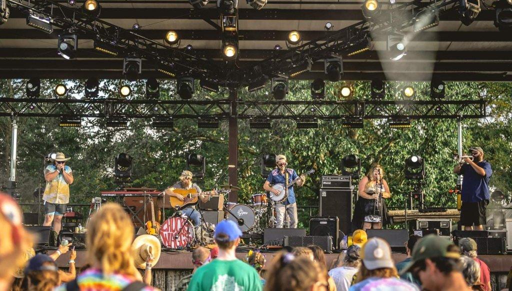 Outdoor concert with a band playing on stage, audience watching.