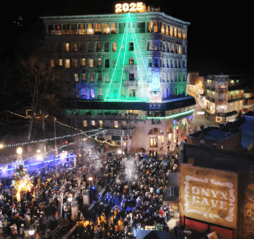 Crowd celebrating outdoors at night with building lit in green, 2023 sign on rooftop.